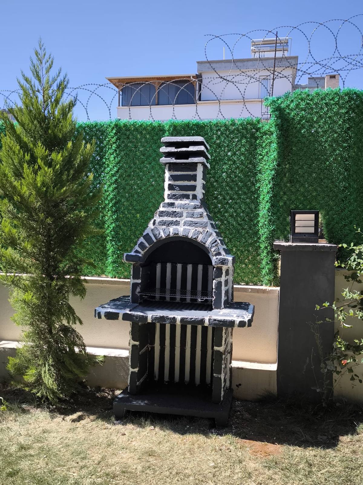 Villa bahçesinde taş desenli barbekü, servi ağaçları arasında